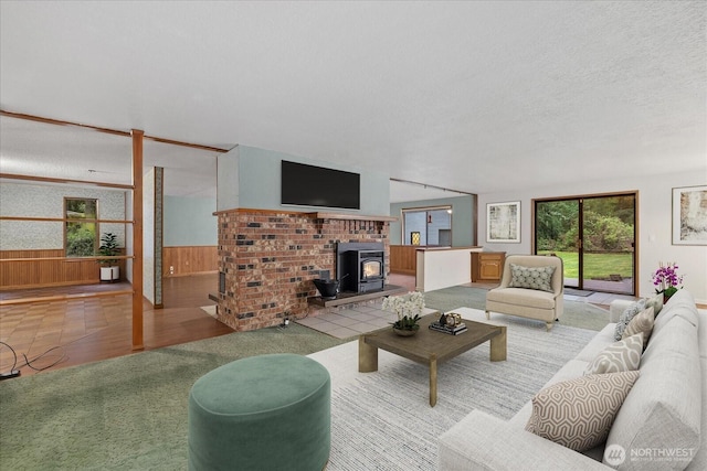 living room with carpet flooring, a wood stove, a textured ceiling, wood walls, and a wainscoted wall