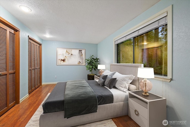 bedroom with wood finished floors, a textured ceiling, and two closets