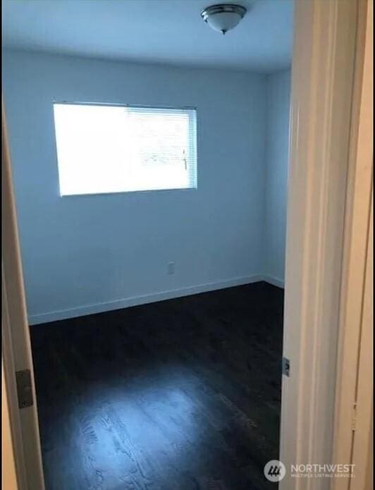empty room with baseboards and dark wood-type flooring