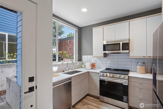 kitchen with light countertops, appliances with stainless steel finishes, decorative backsplash, and a sink