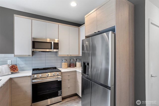 kitchen with light countertops, backsplash, stainless steel appliances, and light wood-style flooring