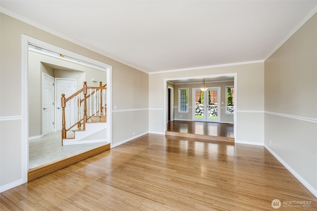 empty room featuring light wood finished floors, stairway, baseboards, and crown molding