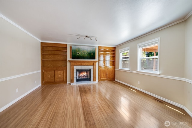 unfurnished living room with a tiled fireplace, baseboards, light wood finished floors, and crown molding