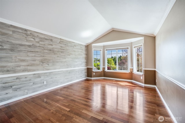 unfurnished room with wood finished floors, vaulted ceiling, ornamental molding, and baseboards