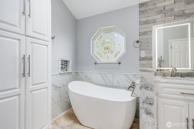 bathroom featuring tile walls, a soaking tub, vanity, and a wainscoted wall