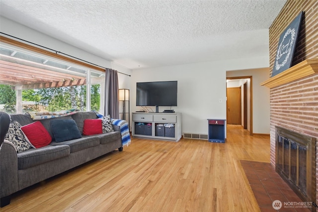 living area with visible vents, a textured ceiling, a brick fireplace, and wood finished floors