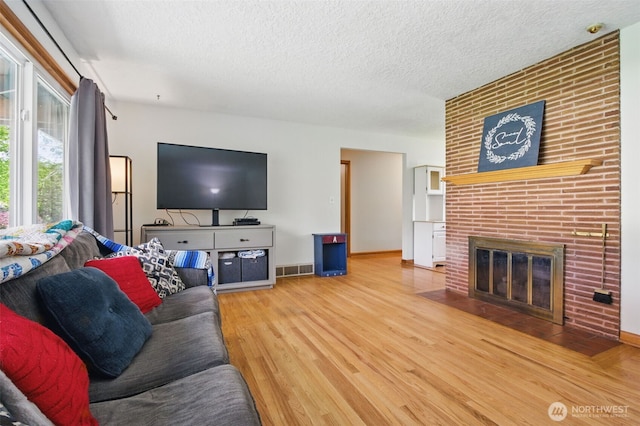 living area with visible vents, wood finished floors, a fireplace, baseboards, and a textured ceiling