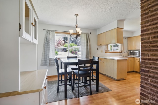 kitchen featuring light brown cabinetry, light wood-type flooring, stainless steel microwave, a peninsula, and a notable chandelier