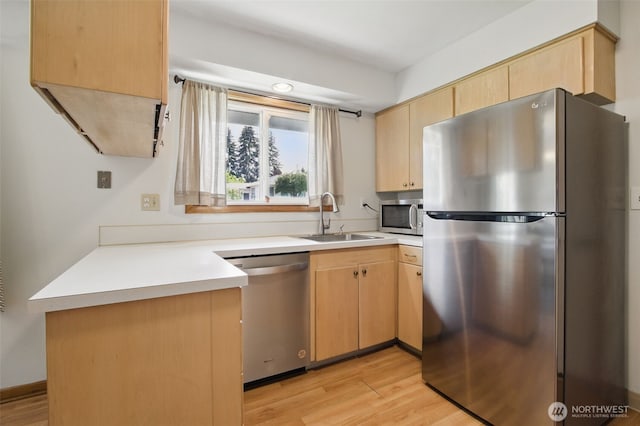 kitchen featuring a sink, light wood finished floors, a peninsula, light brown cabinets, and stainless steel appliances