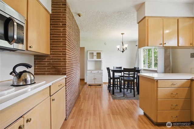 kitchen featuring light countertops, stainless steel microwave, light wood finished floors, an inviting chandelier, and light brown cabinets