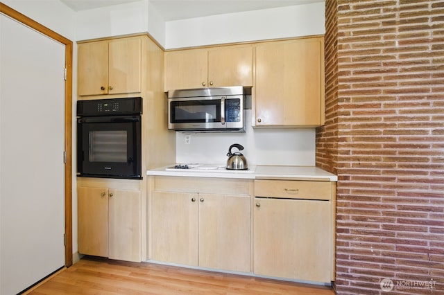 kitchen with light brown cabinetry, oven, light countertops, stainless steel microwave, and light wood-style flooring