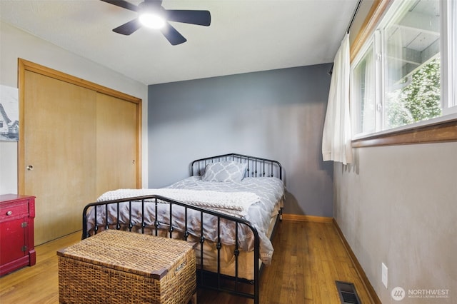 bedroom with a ceiling fan, baseboards, wood finished floors, visible vents, and a closet