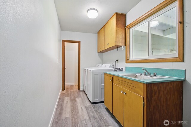 laundry room with baseboards, cabinet space, washing machine and clothes dryer, a sink, and light wood-style flooring