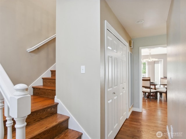 stairs with baseboards, wood finished floors, and a chandelier