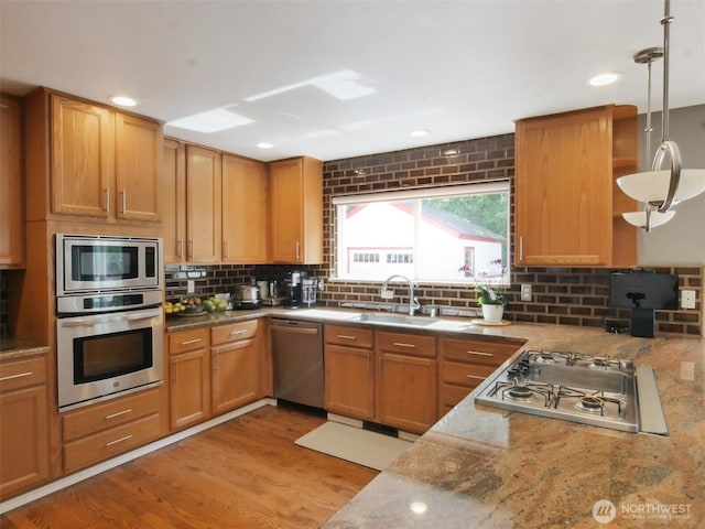 kitchen with decorative backsplash, wood finished floors, a sink, appliances with stainless steel finishes, and hanging light fixtures