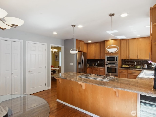 kitchen featuring dark wood-style flooring, a peninsula, stone counters, backsplash, and stainless steel appliances