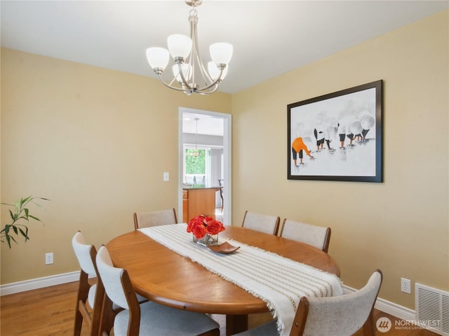 dining area featuring baseboards, a notable chandelier, light wood-style flooring, and visible vents