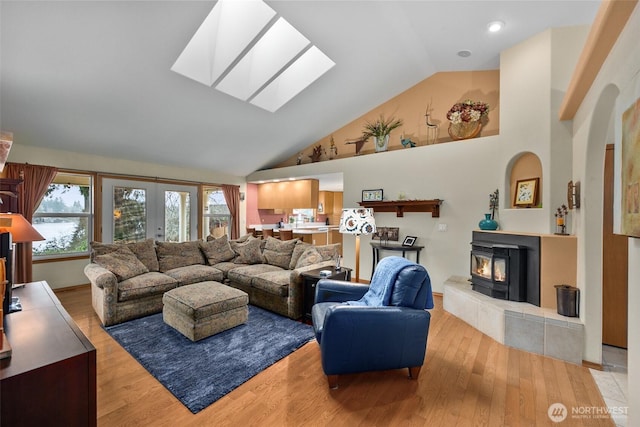 living area featuring a wood stove, a skylight, wood finished floors, and high vaulted ceiling