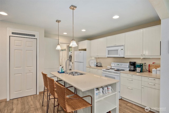 kitchen with white appliances, a kitchen bar, light wood-type flooring, light countertops, and a sink