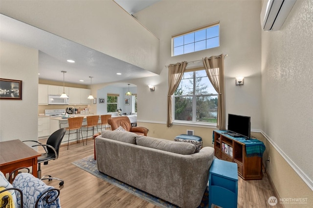 living room featuring a textured wall, arched walkways, light wood-style flooring, a wall unit AC, and a towering ceiling
