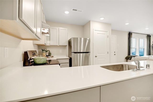 kitchen with visible vents, freestanding refrigerator, extractor fan, light countertops, and a sink