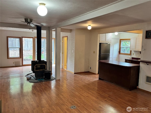 living area with a wood stove, a textured ceiling, a ceiling fan, baseboards, and wood finished floors