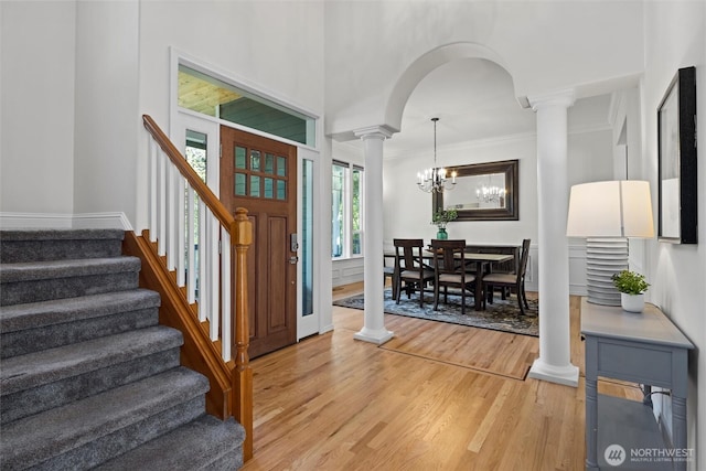 entrance foyer with crown molding, an inviting chandelier, stairway, ornate columns, and light wood finished floors