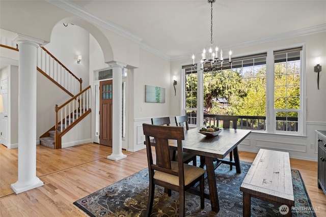 dining space featuring crown molding, a chandelier, stairs, light wood-type flooring, and ornate columns