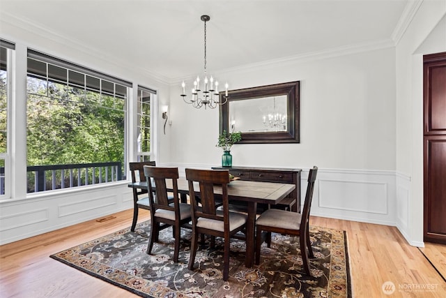 dining area featuring light wood-style floors, wainscoting, an inviting chandelier, ornamental molding, and a decorative wall