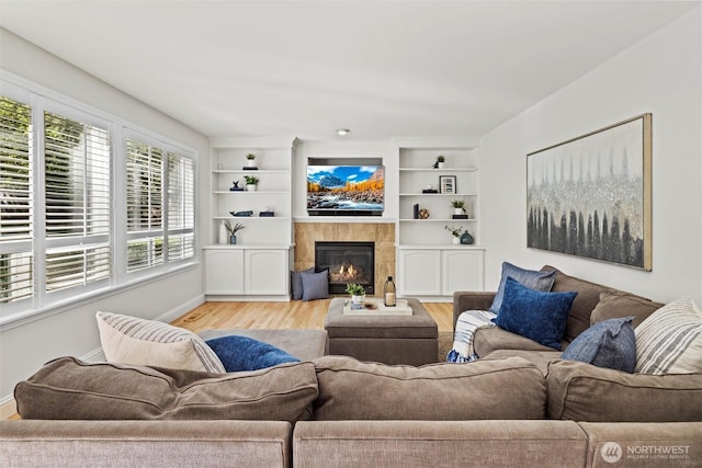 living area featuring light wood-type flooring, baseboards, built in shelves, and a fireplace
