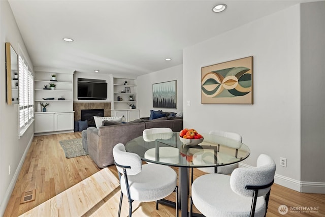 dining area with baseboards, visible vents, light wood-type flooring, and a fireplace