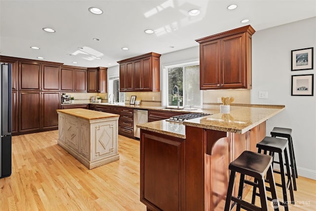 kitchen featuring recessed lighting, a sink, light wood finished floors, and a peninsula