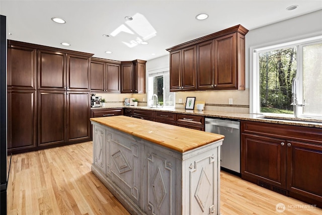 kitchen featuring stainless steel dishwasher, light wood-style flooring, butcher block counters, and a wealth of natural light