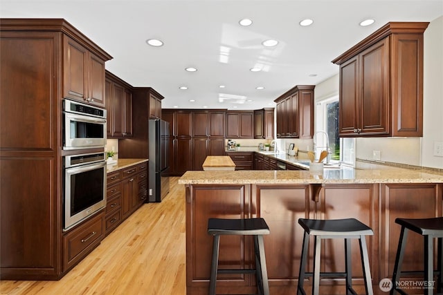 kitchen with recessed lighting, freestanding refrigerator, a peninsula, and light wood-type flooring