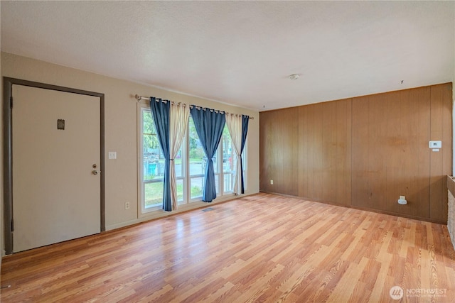 unfurnished living room with light wood-style floors and wooden walls