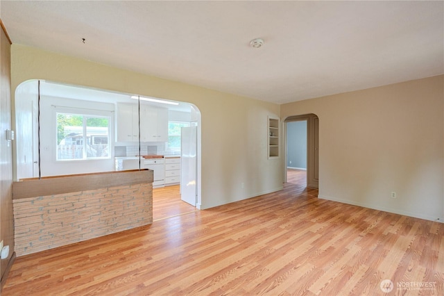 empty room with arched walkways, light wood-style floors, and a smoke detector