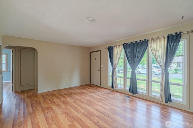 unfurnished room with light wood-type flooring, arched walkways, and baseboards