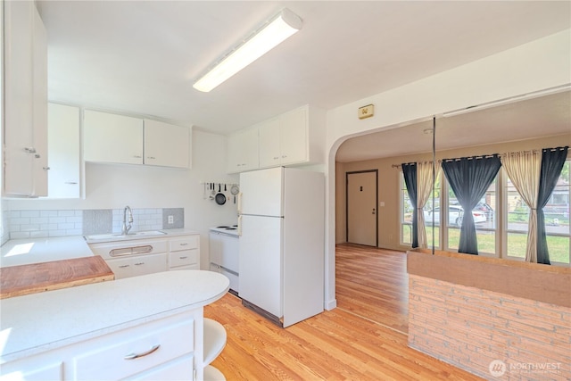 kitchen with white appliances, a sink, light countertops, light wood-style flooring, and backsplash