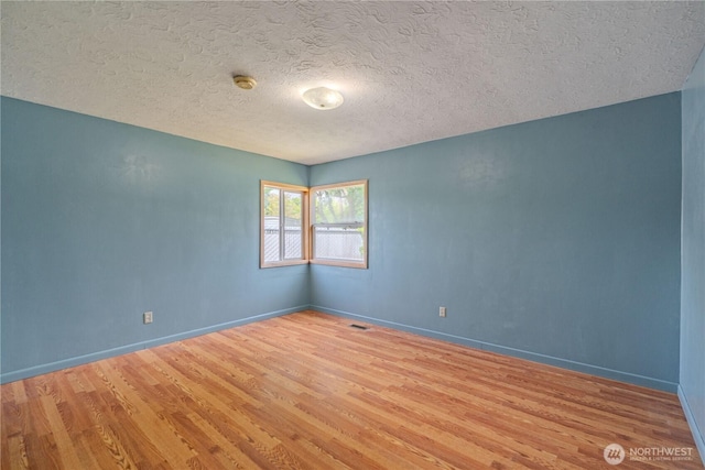 empty room with wood finished floors, a textured ceiling, baseboards, and a smoke detector
