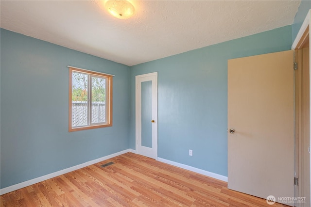 spare room featuring light wood finished floors, baseboards, and a textured ceiling