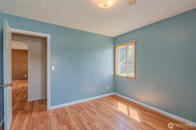 unfurnished room featuring wood finished floors, arched walkways, baseboards, and a textured ceiling