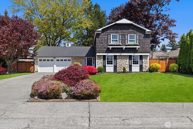 dutch colonial with a garage, a front lawn, fence, stone siding, and driveway