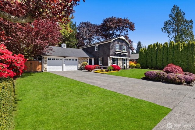 view of front facade featuring fence, an attached garage, stone siding, a front yard, and concrete driveway