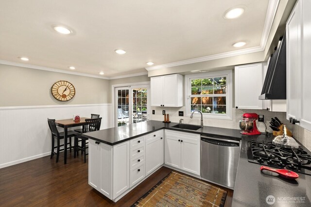 kitchen with a peninsula, dark countertops, white cabinets, a sink, and dishwasher