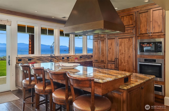 5844 Mutiny Bay Rd, Freeland, WA 98249 - kitchen with island exhaust hood, brown cabinetry, appliances with stainless steel finishes, and a wealth of natural light