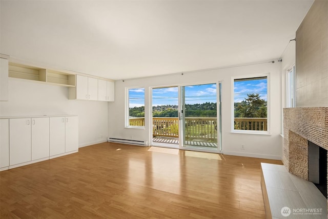 unfurnished living room featuring baseboard heating, light wood finished floors, a tiled fireplace, and baseboards