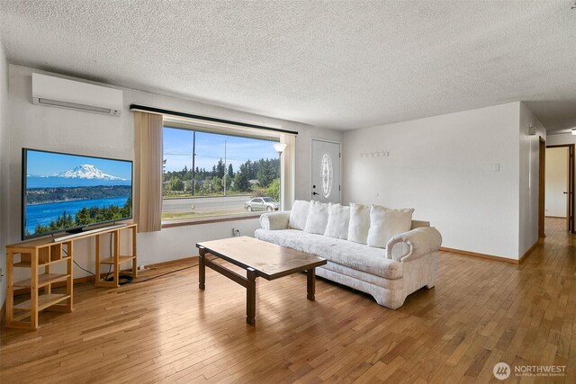 living room with baseboards, a textured ceiling, a wall mounted AC, and hardwood / wood-style flooring