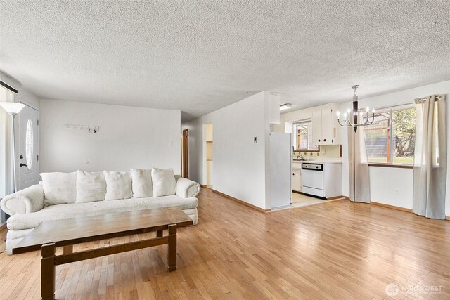 living area with an inviting chandelier, a textured ceiling, light wood-style floors, and baseboards