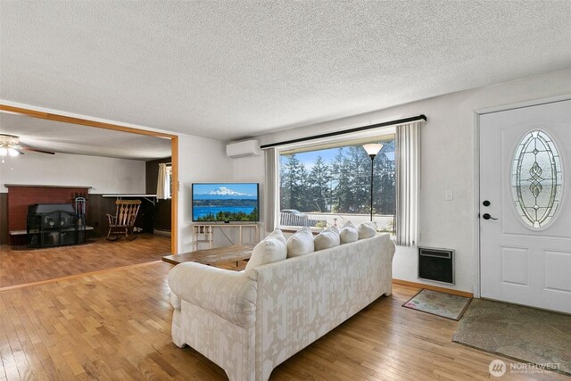 living room with a textured ceiling, a ceiling fan, heating unit, a wall unit AC, and hardwood / wood-style flooring