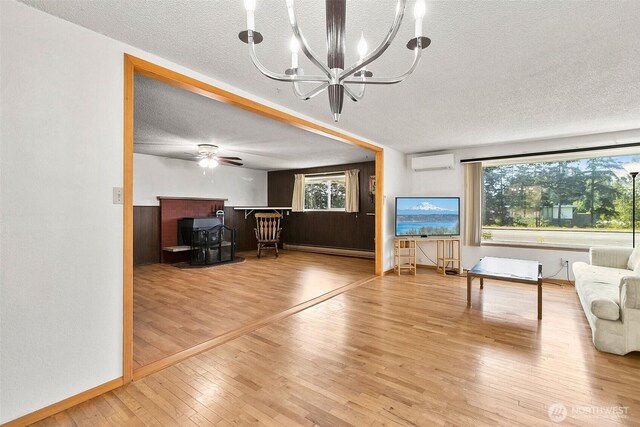 living area featuring wood finished floors, an AC wall unit, a textured ceiling, a baseboard radiator, and ceiling fan with notable chandelier